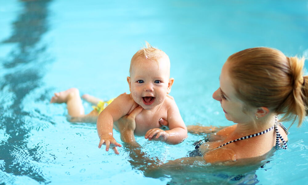 Eine Mutter, die ihr lachendes Baby im Schwimmbecken hält