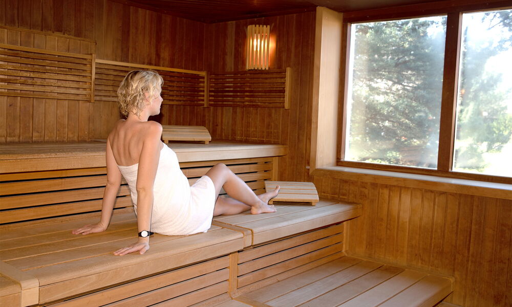 Eine Frau in der finnischen Sauna, die durch ein Fenster in den Saunagarten schaut