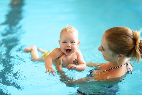 Eine Mutter, die ihr lachendes Baby im Schwimmbecken hält